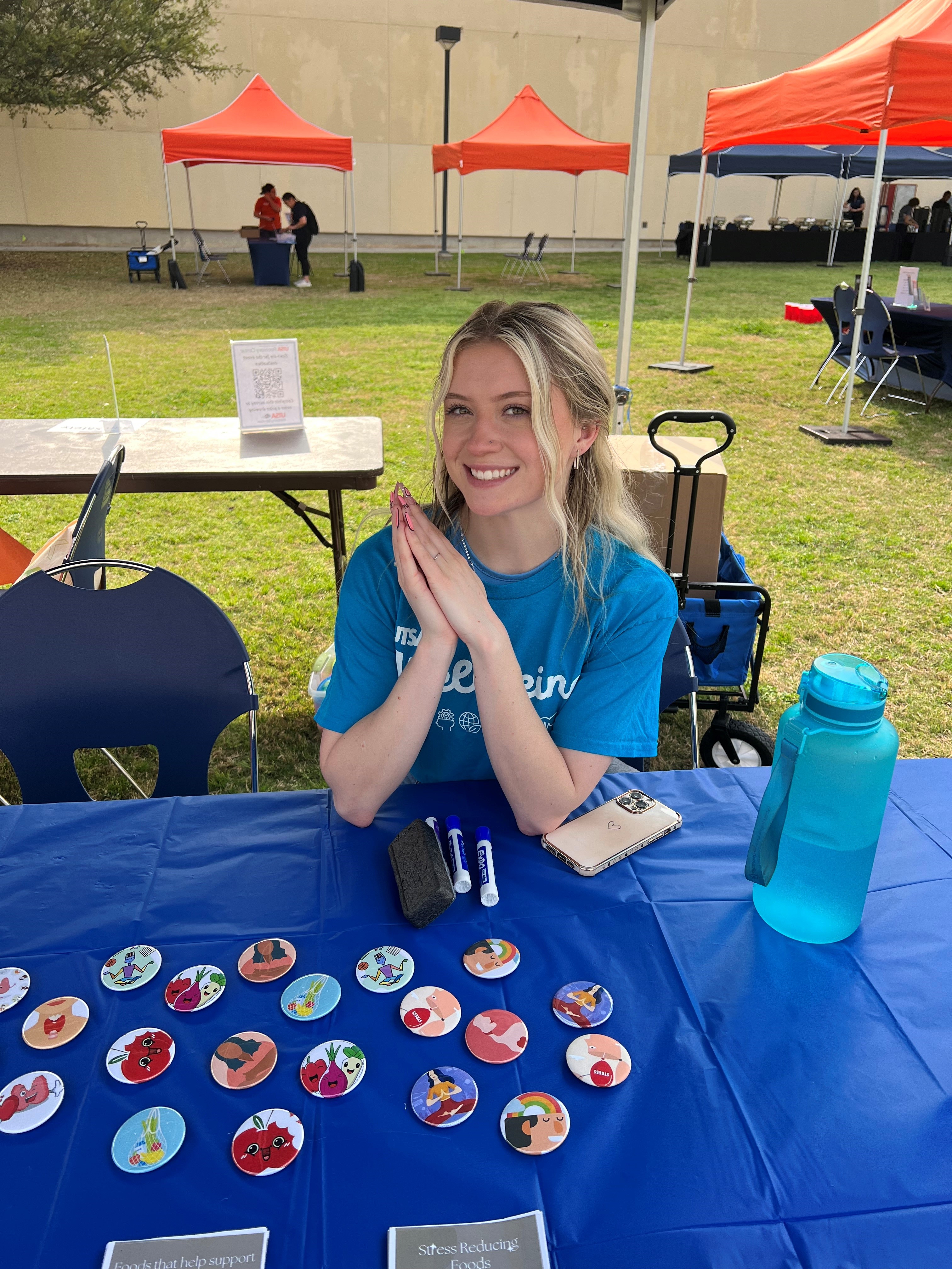 UTSA Student Tabling with Buttons on table, wearing a blue Wellbeing shirt
